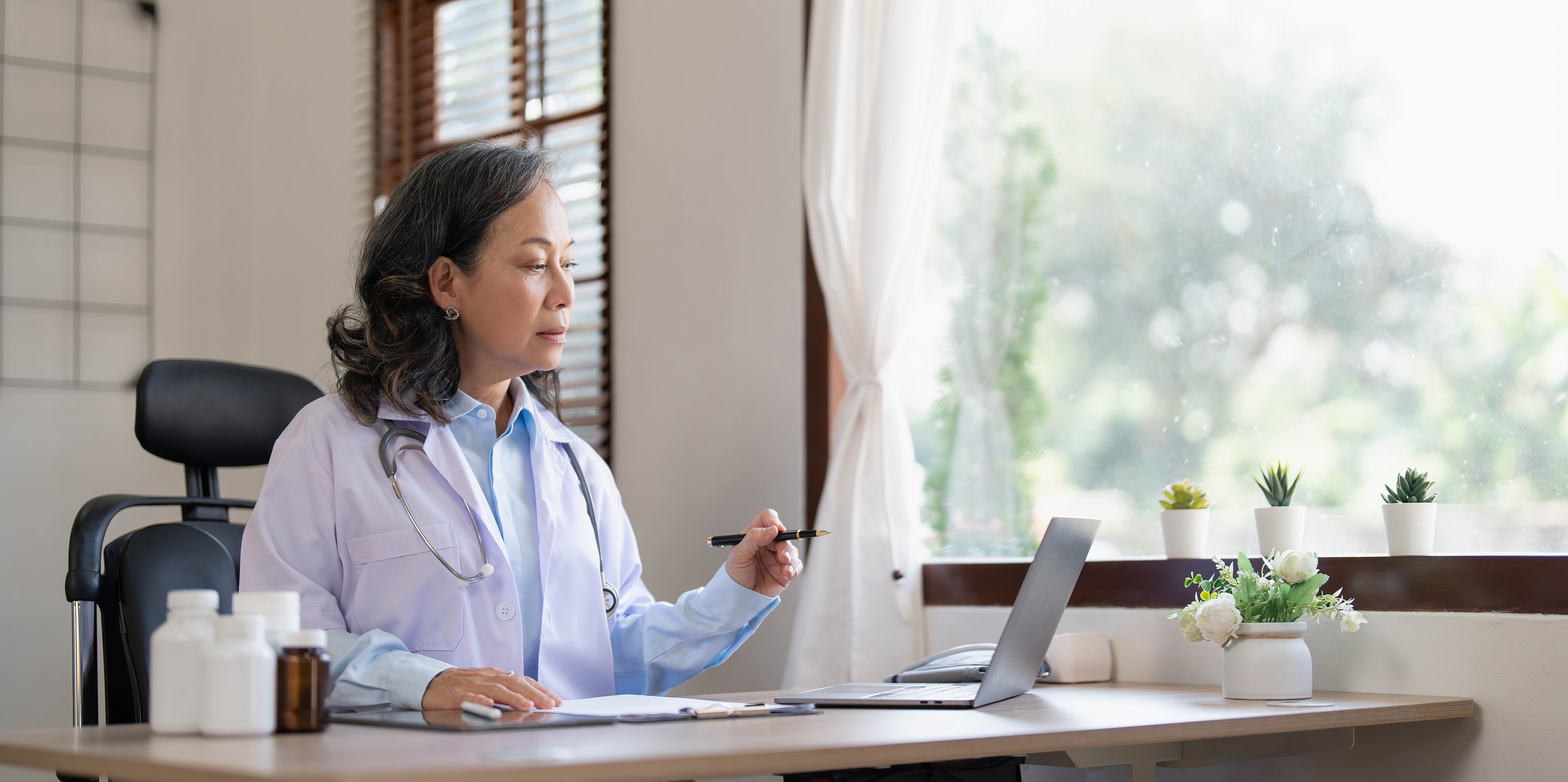 A medical professional looking at a laptop holding a pen